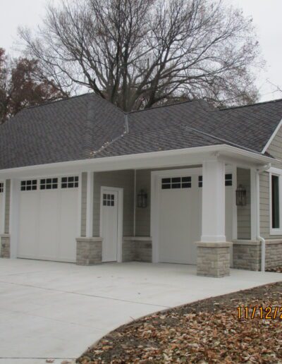 Newly built single-story house with a double garage and a covered porch, surrounded by bare trees.