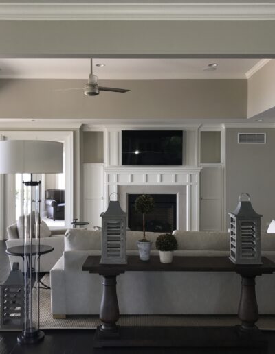 A modern living room with neutral tones, featuring a fireplace, seating area, and large windows.