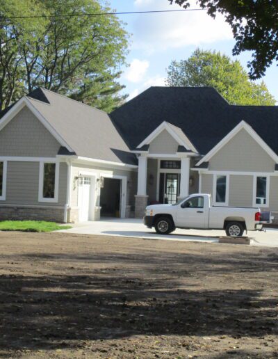 A white pickup truck parked in front of a newly constructed house with a waterfront view.
