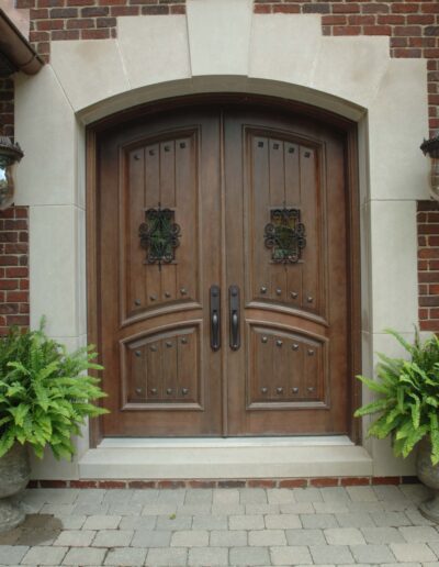 Ornate wooden double doors with decorative ironwork, flanked by potted ferns.