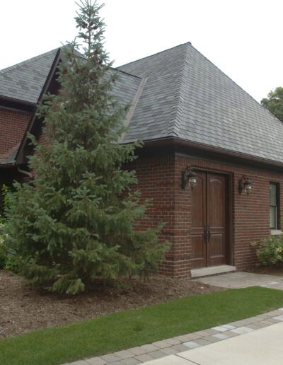A red brick house with a sloping shingle roof, complemented by a landscaped garden and a basketball hoop in the background.