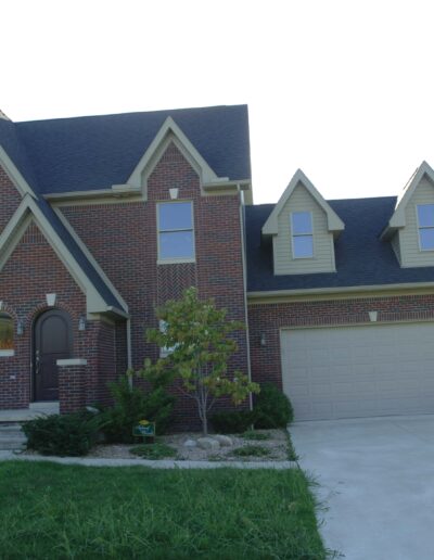 A brick two-story house with an attached garage and a driveway in a residential area.