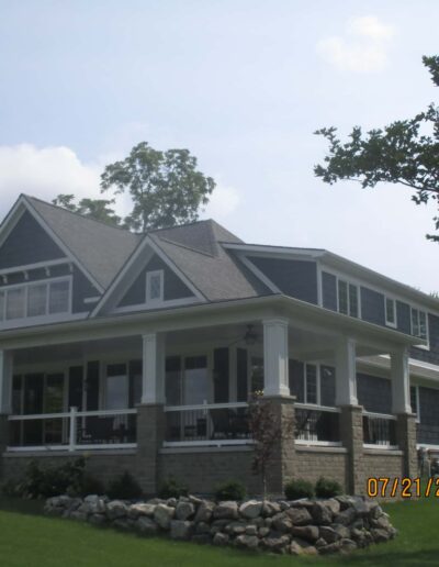 Large two-story house with a wraparound porch and stone accents, photographed on a sunny day.