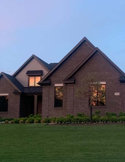 Suburban home captured at dusk with illuminated windows and a well-manicured lawn.
