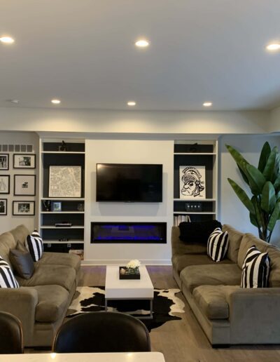 A modern living room with two sofas, a television, and a fireplace, decorated with wall art and plants.