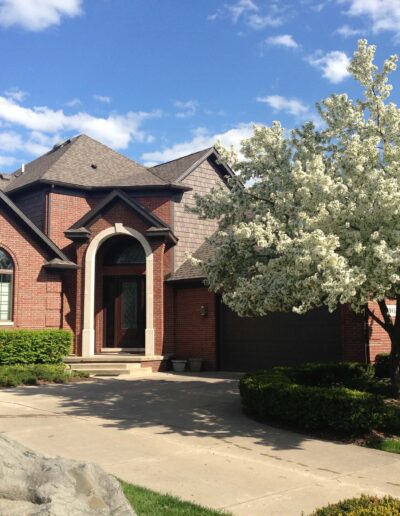 A suburban brick house with blossoming trees on a sunny day.