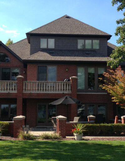 A two-story brick house with a balcony, patio, and landscaped front yard.