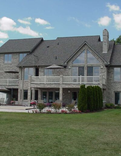 Large two-story stone house with a balcony, manicured lawn, and clear skies.
