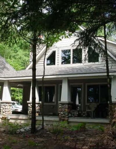 A two-story house with stone foundations, white siding, and a surrounding woodland.