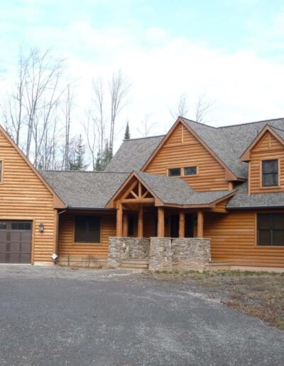 A large wooden house with a two-car garage and gabled roofs on a cloudy day.