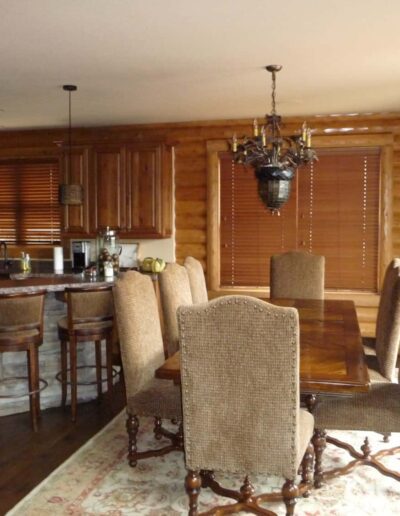 Rustic dining room with a wooden table, upholstered chairs, and a kitchen bar in the background.